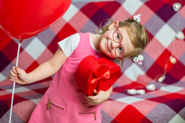 Piccola bella ragazza in bicchieri con cuore rosso scatola regalo e palloncino