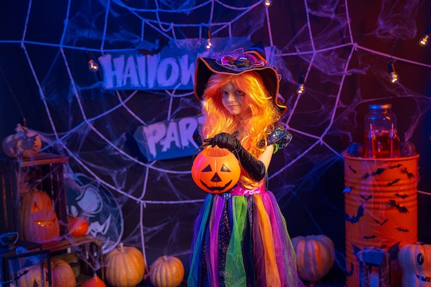 Piccola bella ragazza in un costume da strega celebra la festa di Halloween felice all'interno con le zucche