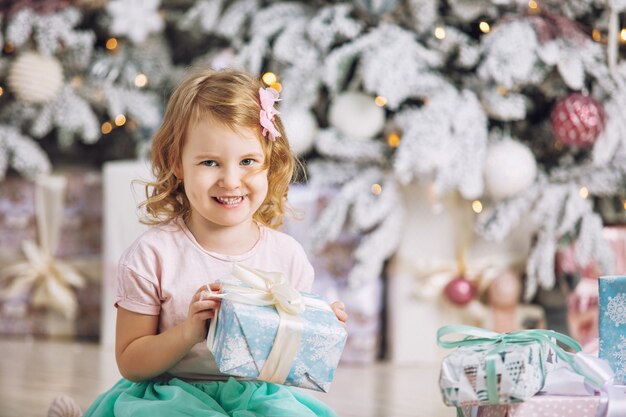 Piccola bellissima bambina con un regalo allegro e alla moda nell'interno natalizio della casa