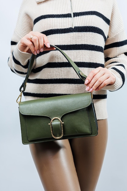 Piccola borsa in pelle verde in una mano femminile su sfondo bianco Borsa a tracolla Una donna con una borsetta verde Stile moda vintage ed eleganza