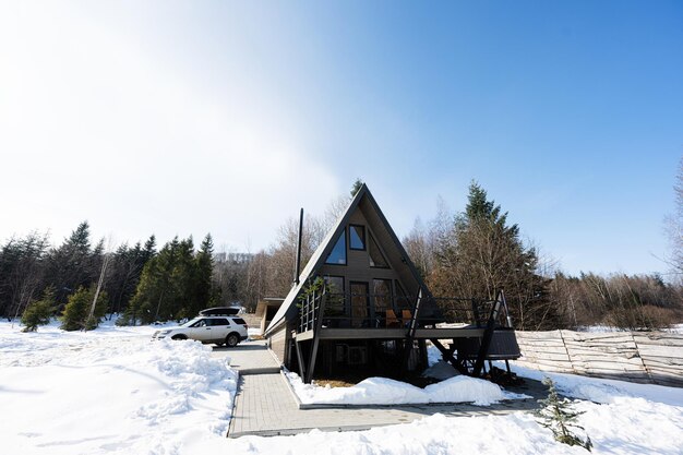 Piccola cabina di campagna in legno triangolare con vasca idromassaggio e auto suv con portapacchi in montagna Fine settimana dell'anima