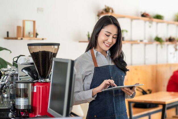 Piccola caffetteria di proprietà Una donna asiatica utilizza un tablet e una tecnologia nel campo del servizio.