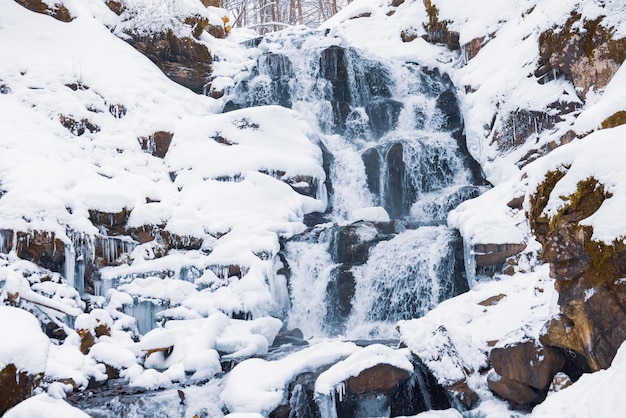 Piccola cascata di acqua fredda scorre tra le pietre coperte di neve