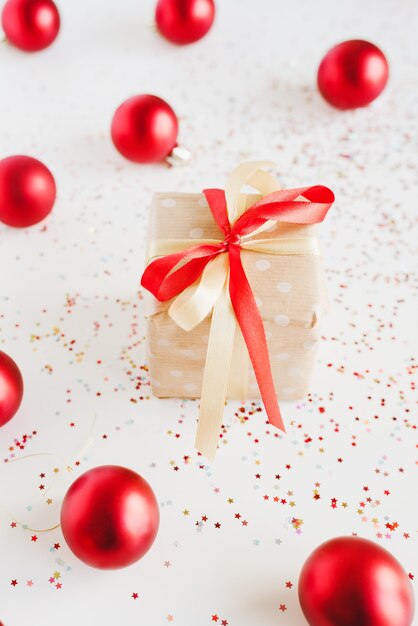 Piccola confezione regalo avvolta in carta kraft a pois, palle di Natale e coriandoli su sfondo bianco