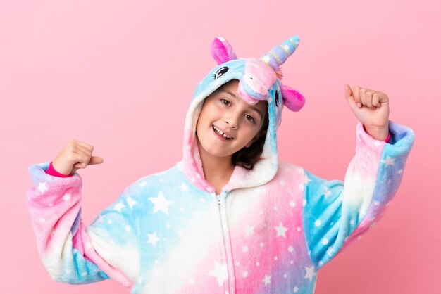 Piccola donna caucasica che indossa un pigiama unicorno isolato su sfondo rosa che celebra una vittoria