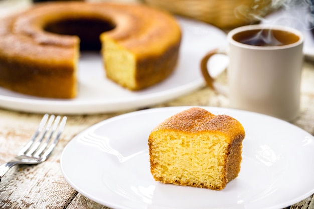 Piccola fetta di torta di farina di mais, tipica torta rurale brasiliana a base di farina di mais, con caffè caldo sullo sfondo, colazione brasiliana