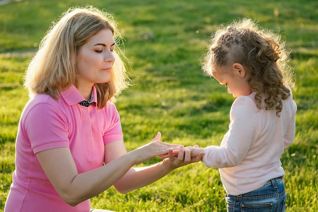 Piccola figlia bionda sveglia in un vestito blu con la bella madre che applica il gel antibatterico antisettico nel giorno di estate nel fondo dell'erba dei verdi del campo. protezione dai germi al picnic