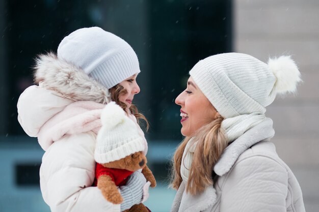 Piccola figlia guardando la madre e tenendo l'orsacchiotto nella città invernale