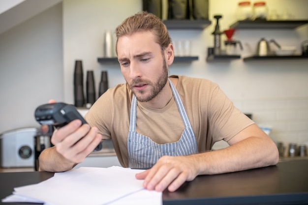 Piccola impresa. Intelligente giovane barbuto uomo concentrato in grembiule che conta i profitti e le spese del suo caffè