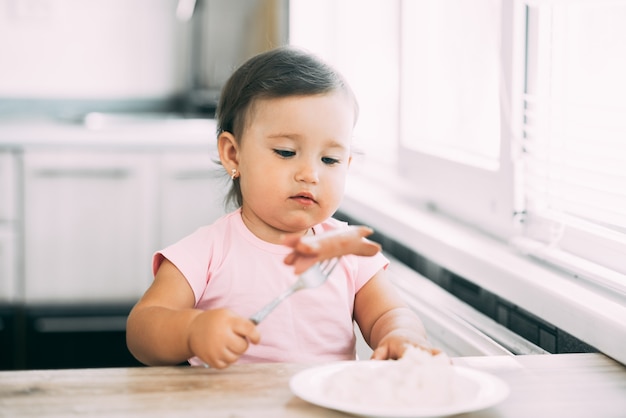 Piccola neonata in cucina che mangia salsiccia e purè di patate