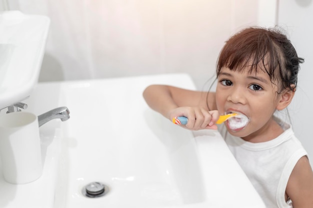 Piccola neonata sveglia che si pulisce i denti con uno spazzolino da denti in bagno