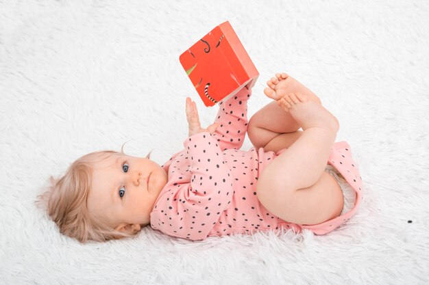 Piccola neonata sveglia con il libro nella camera da letto del genitore.