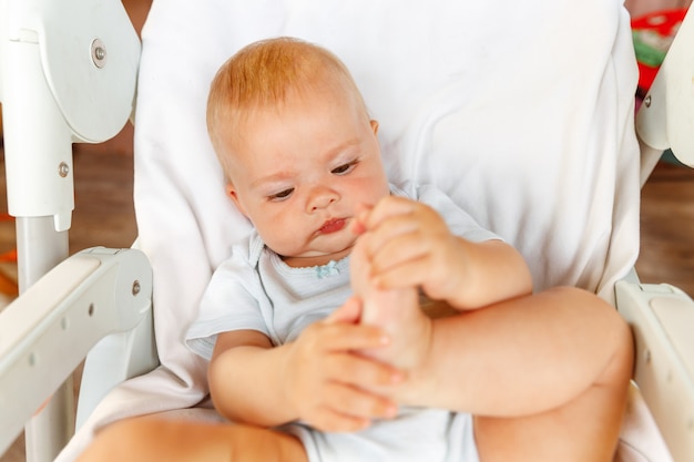 Piccola neonata sveglia con la faccia sorridente che guarda l'obbiettivo su priorità bassa bianca. Neonato che riposa giocando sdraiato sulla sedia di alimentazione a casa. Concetto di maternità bambino felice.