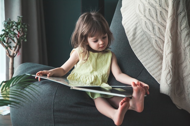 Piccola neonata sveglia in vestito giallo che legge un libro a casa, seduto su un sacchetto di fagioli