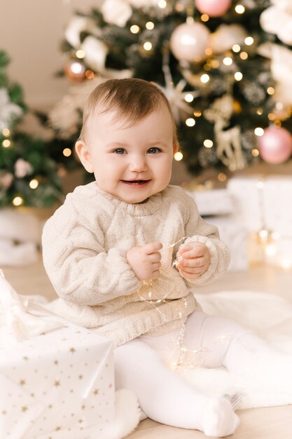 Piccola neonata sveglia sotto l'albero di Natale. Buone vacanze, felice anno nuovo. Periodo natalizio