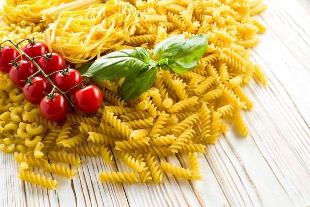 Piccola pasta per zuppe, pasta riccia e foglia di basilico con pomodori sul tavolo