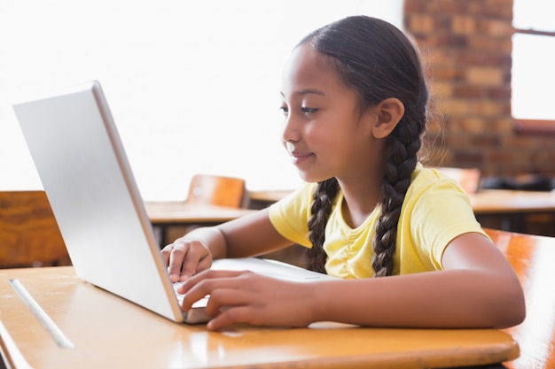 Piccola pupilla sveglia che esamina computer portatile nell&#39;aula