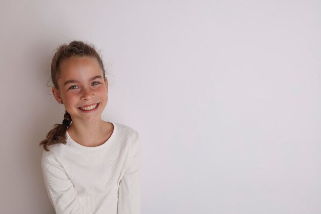 Piccola ragazza adolescente emotiva in camicia bianca 11 12 anni su uno sfondo bianco isolato Ritratto in studio per bambini Posizionare il testo per copiare lo spazio per l39iscrizione pubblicità merci per bambini