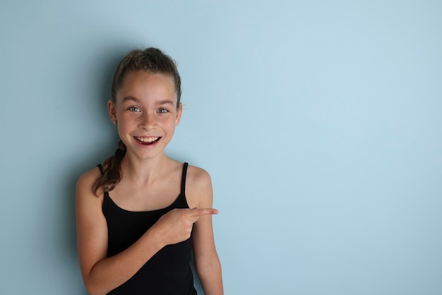 Piccola ragazza adolescente emotiva in una maglietta nera 11 12 anni su uno sfondo blu isolato Ritratto in studio per bambini Posiziona il testo per copiare il posto per l'iscrizione