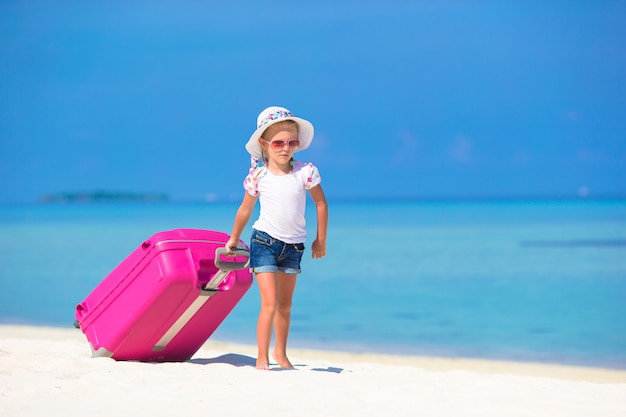 Piccola ragazza adorabile con grande valigia sulla spiaggia bianca tropicale