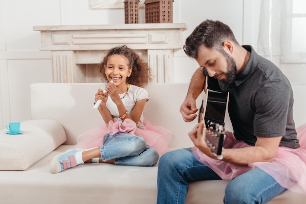Piccola ragazza afroamericana che canta mentre il padre suona la chitarra a casa