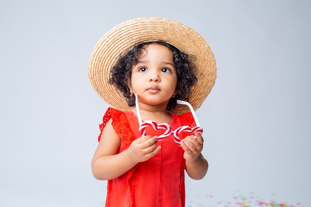 piccola ragazza afroamericana in abiti estivi rossi e un cappello di paglia su uno sfondo bianco in studio