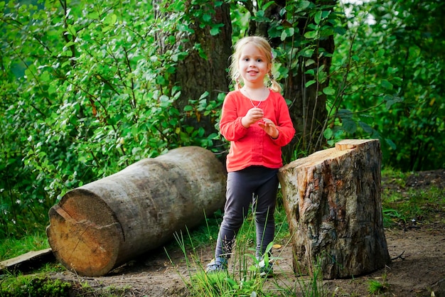 piccola ragazza allegra è seduta su un tronco nella foresta.