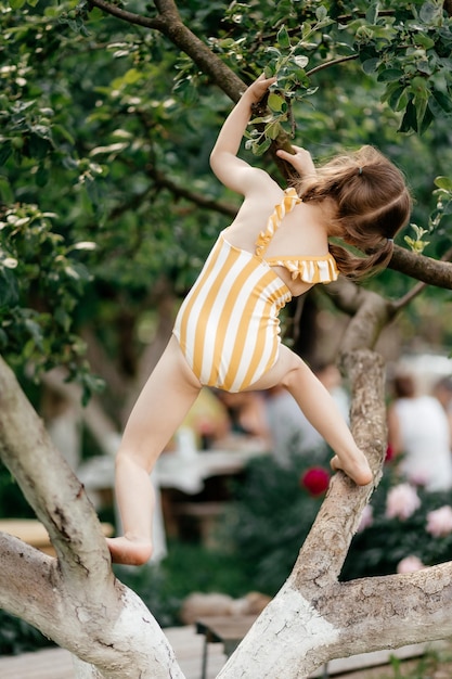 Piccola ragazza arrampicarsi sull'albero in estate attività del giardino Bambina sul ramo di albero infanzia Attività di vacanza stile di vita