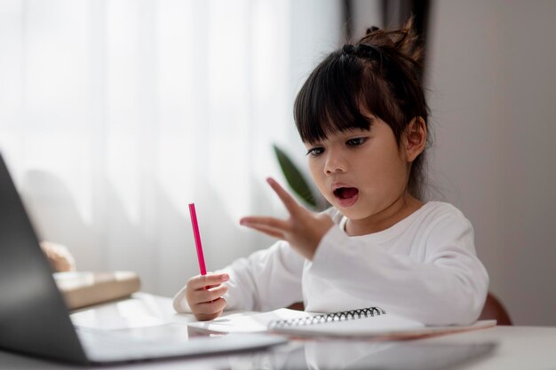 Piccola ragazza asiatica che fa i compiti con il computer portatile