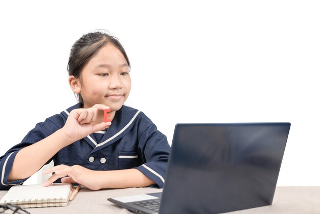 Piccola ragazza asiatica che fa i compiti sul computer portatile