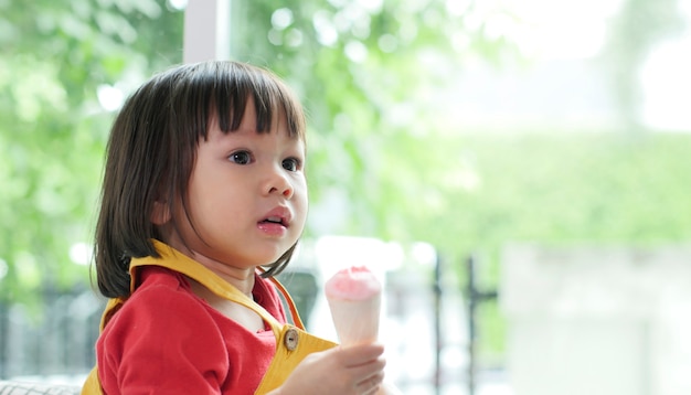 Piccola ragazza asiatica che mangia il gelato in un cono croccante