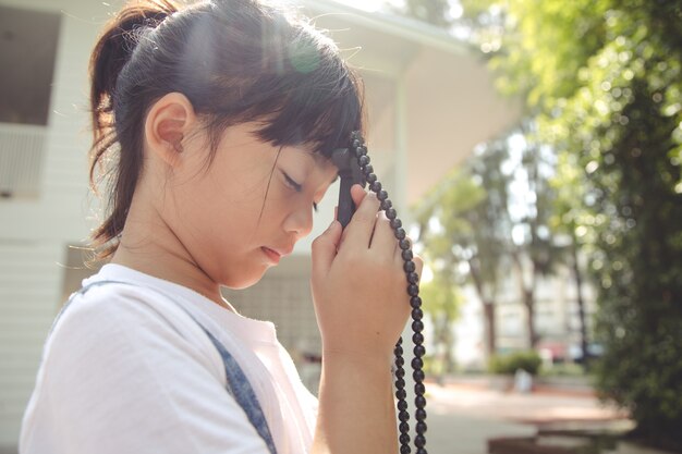 Piccola ragazza asiatica che prega tenendo la croce, concetto cristiano.