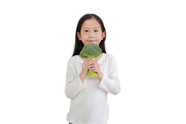 Piccola ragazza asiatica che tiene i broccoli isolati su sfondo bianco. Concetto di capretto e verdura. Concentrati sui broccoli nelle mani