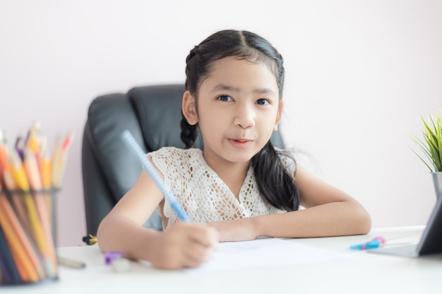 Piccola ragazza asiatica che usa la matita per scrivere sulla carta facendo i compiti e sorride con felicità per il concetto di educazione seleziona la messa a fuoco poca profondità di campo