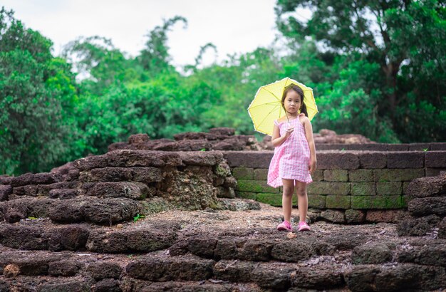 Piccola ragazza asiatica con lo standind giallo dell'ombrello sulla roccia del Th del sito storico in Tailandia