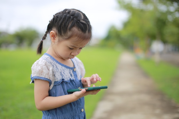 Piccola ragazza asiatica con uno smartphone all'aperto.