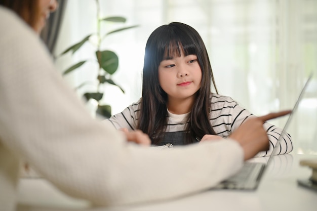Piccola ragazza asiatica concentrata che studia inglese a casa con sua madre che guarda lo schermo del laptop