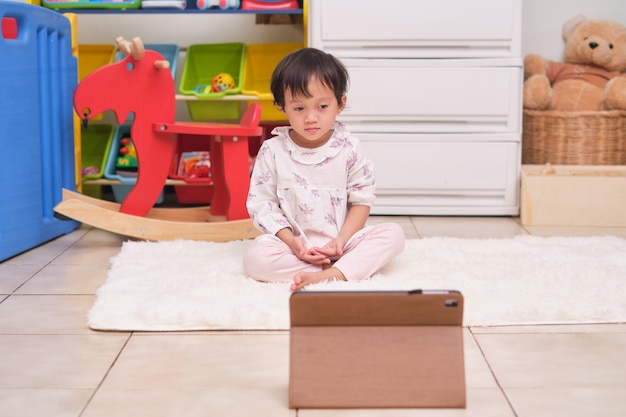 Piccola ragazza asiatica di 2 anni pratica yoga e meditazione con formazione online su tablet a casa, meditazione per principianti, esercizi di respirazione per bambini