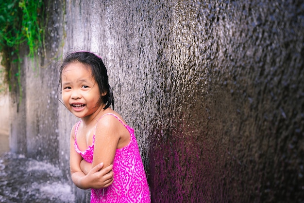 Piccola ragazza asiatica felice che ritiene fredda mentre giocando acqua in canale di scarico della diga