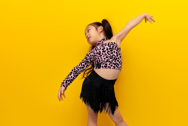 Piccola ragazza asiatica in abito da ballo balla chachacha su sfondo giallo isolato ballerino bambino coreano