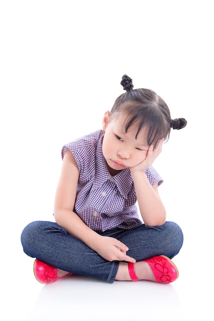 Piccola ragazza asiatica infelice che si siede sul pavimento isolato sopra fondo bianco