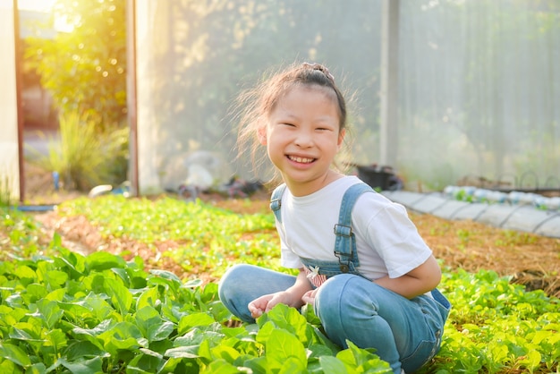 Piccola ragazza asiatica seduta e sorridente in serra.