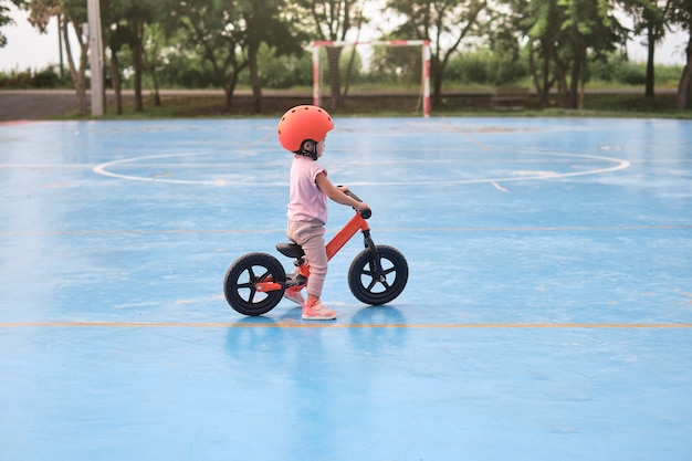 Piccola ragazza asiatica sveglia che indossa il casco di sicurezza mentre impara ad andare in bicicletta