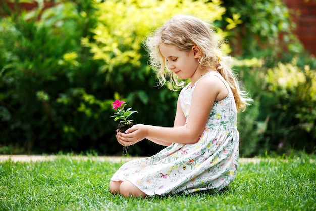 Piccola ragazza bionda che tiene in mano una giovane pianta di fiori su sfondo verde