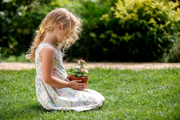 Piccola ragazza bionda che tiene in mano una giovane pianta di fiori su sfondo verde