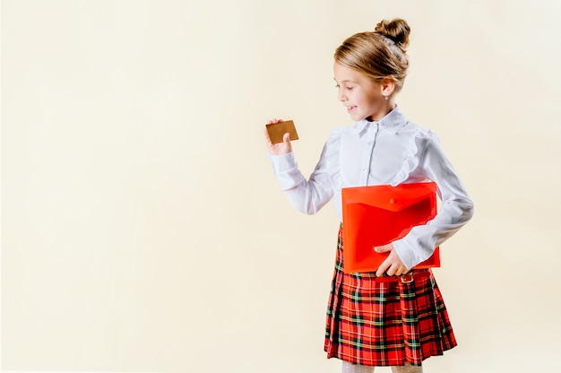 Piccola ragazza bionda che tiene una carta in bianco in uniforme scolastico