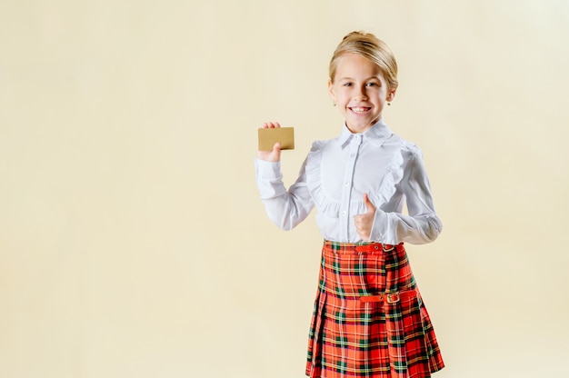 Piccola ragazza bionda che tiene una carta in bianco in uniforme scolastico