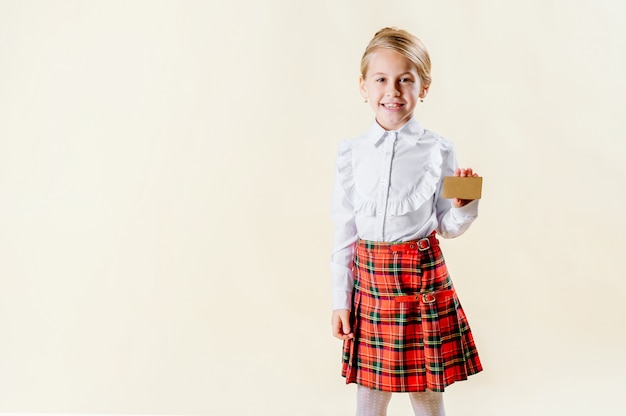 Piccola ragazza bionda che tiene una carta in bianco in uniforme scolastico