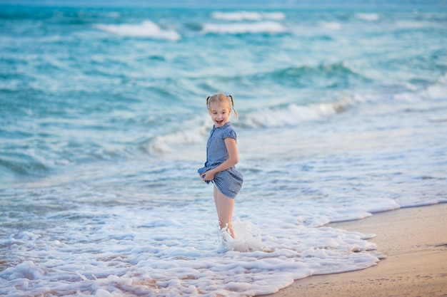 Piccola ragazza bionda in abito blu sul mare