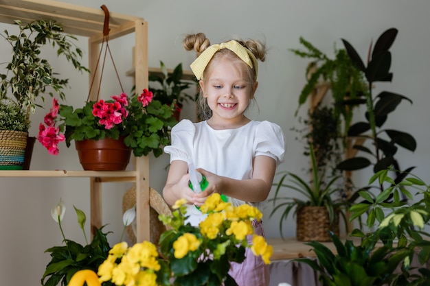 piccola ragazza bionda spruzza da un erogatore di proiettili o innaffia i fiori interni Giardinaggio domestico